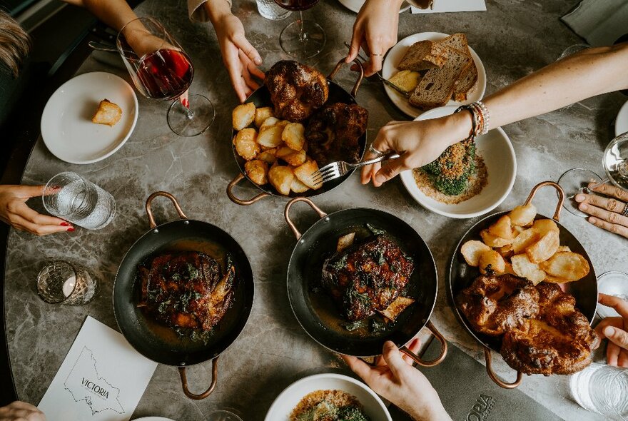 Overhead view looking down onto a table filled with different sized plates and skillets of food, with hands reaching in to select food with utensils.