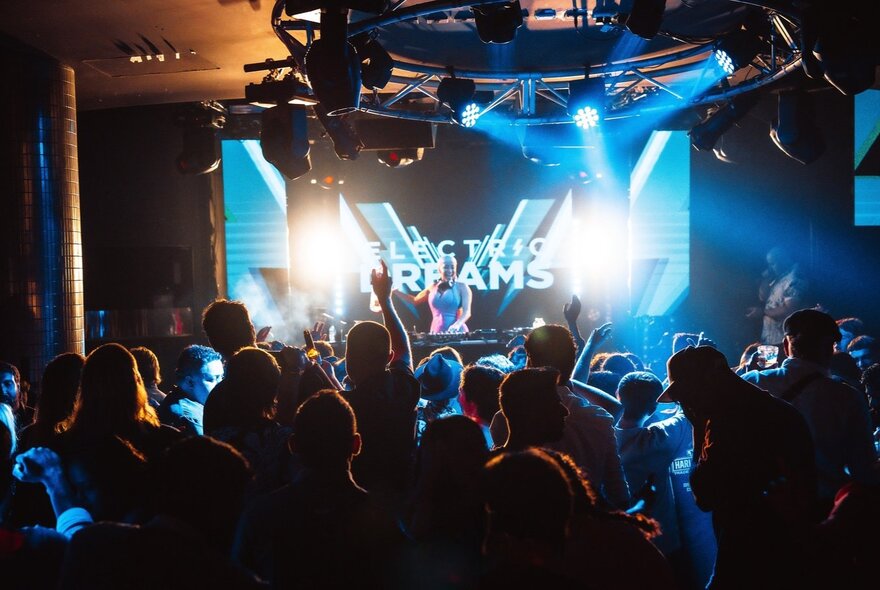 People dancing in a nightclub with a DJ playing music on the stage in front of them.