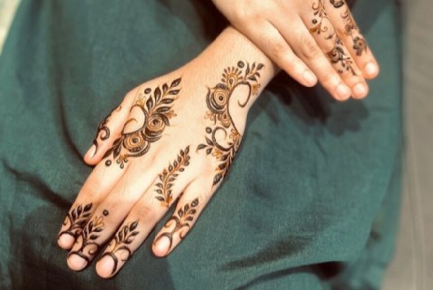 Hands with henna tattoos on a background of green material. 