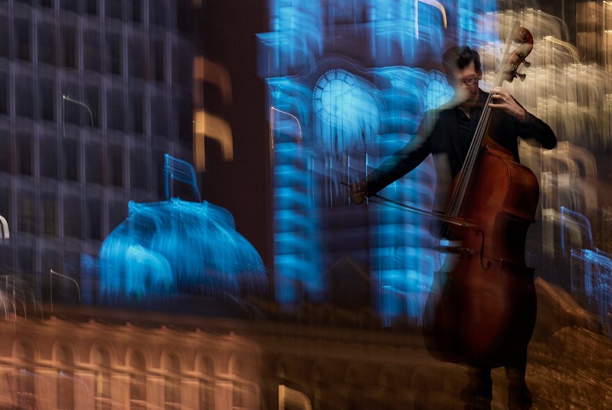 A musician blurred in motion, standing on a stage and playing an upright bass, the background also slightly blurred.