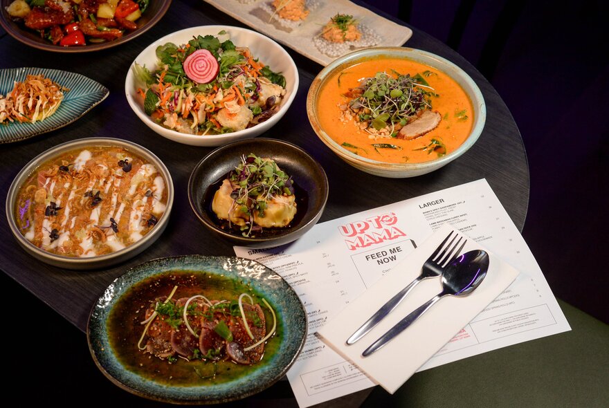 A collection of Asian-style dishes displayed on a black table with a menu and single set of cutlery.