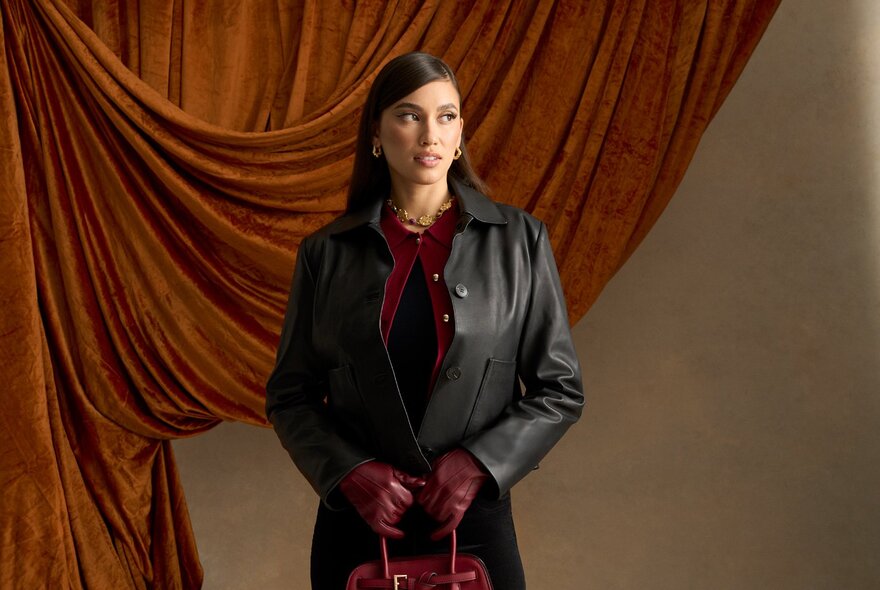 Woman wearing a leather jacket against swag curtains.