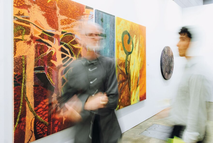 Blurred people looking at bright artwork on a gallery wall.
