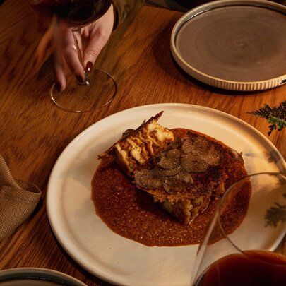 A slice of truffle lasagne with a rich sauce on a white plate, on a dining table.