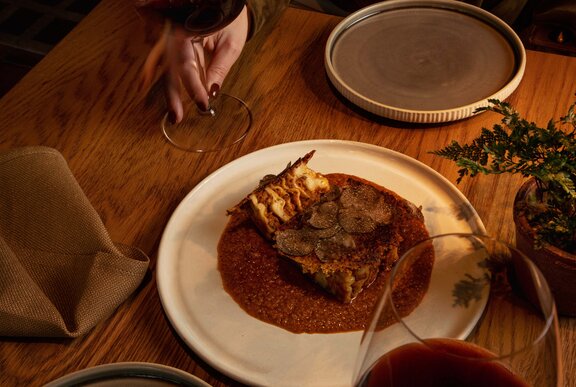 A slice of truffle lasagne with a rich sauce on a white plate, on a dining table.
