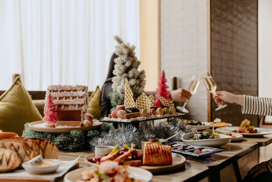 A table at a restaurant filled with plates of Christmas themed food, including a gingerbread house, and a festive centrepiece.