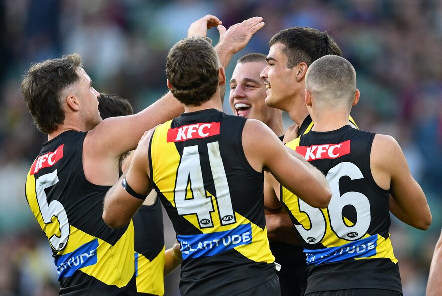 A group of Richmond AFL football players high-fiving and celebrating in a huddle on the field.