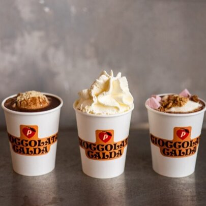 Three takeaway cups of hot chocolate, the middle cup with whipped cream.