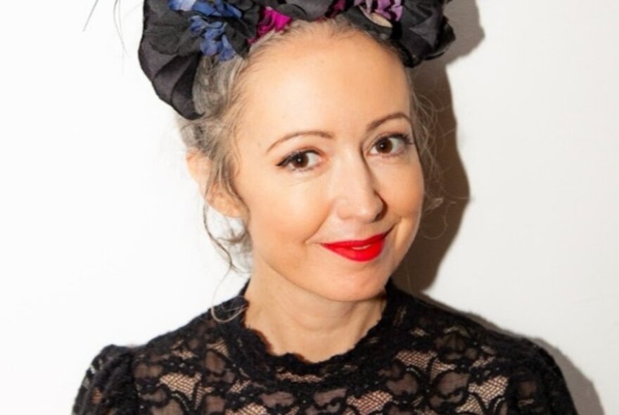 Writer and journalist Marieke Hardy, a woman with a slight smile, wearing red lipstick and a black lace top, her hair arranged with ribbons on top of her head.