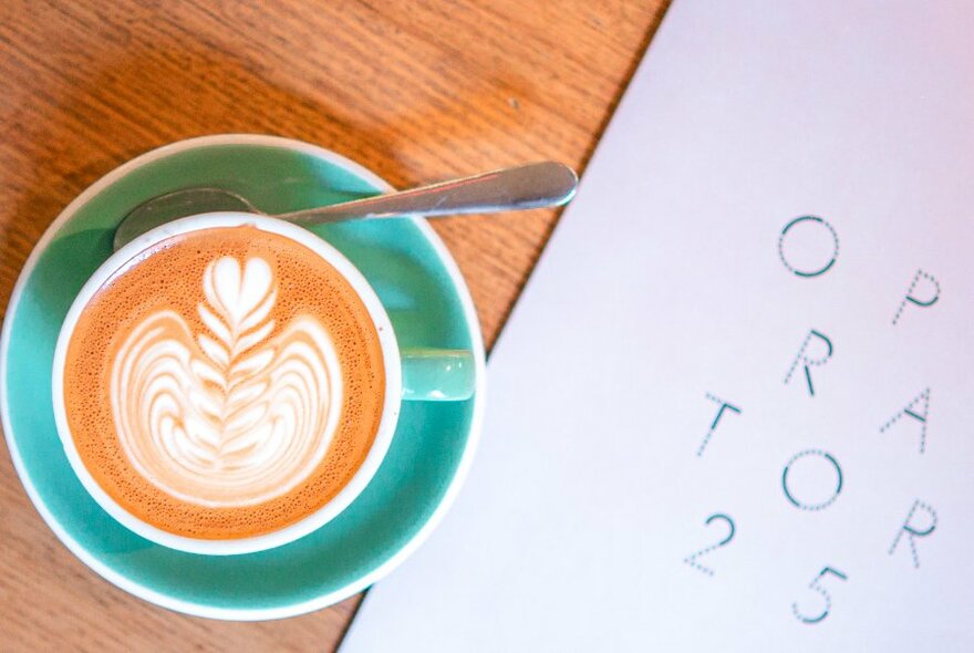 Overhead view of a cup of coffee showing milk froth art, next to a cafe menu.