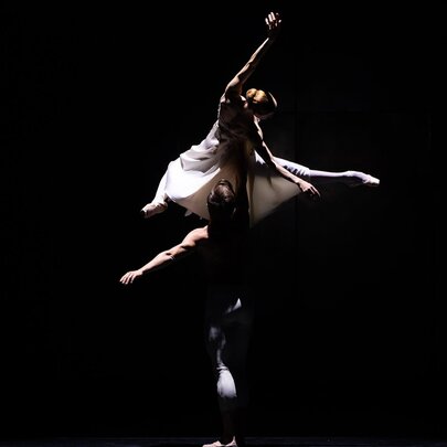 Dramatically lit ballet dancers performing mid-poise with arms and legs stretched.
