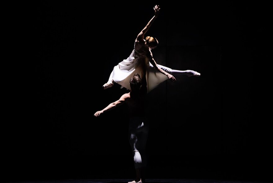Dramatically lit ballet dancers performing mid-poise with arms and legs stretched.