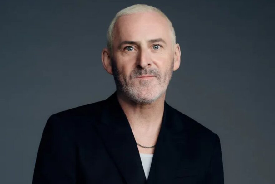 Hairdresser Shay Dempsey sitting looking neutral in a black blazer. 