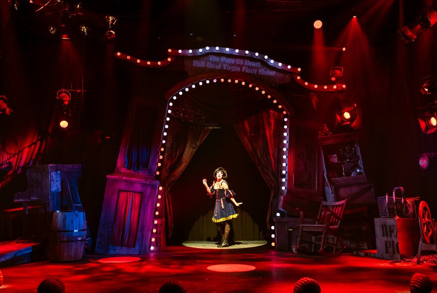 Figure standing on stage under a spotlit arch.