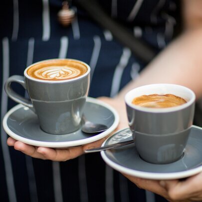 Two hands holding two cups of coffee in grey ceramic cups.