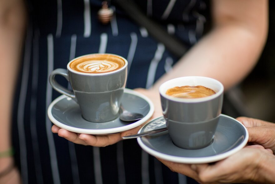 Two hands holding two cups of coffee in grey ceramic cups.