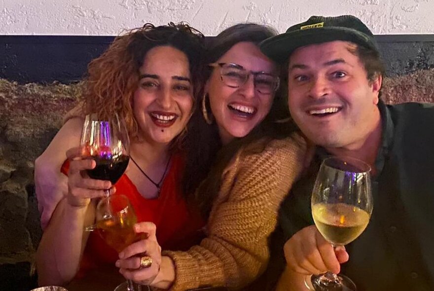 Three people smiling for the camera with glasses of wine.