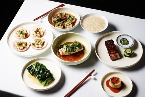 Dishes of Chinese food served on white plates on a white linen covered table.