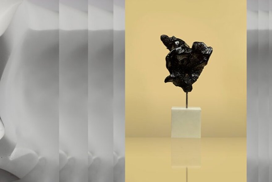 A small, dark, abstract sculpture mounted on a white rectangular base.