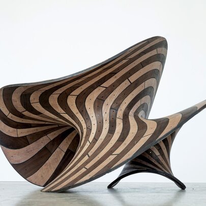A wooden sculpture with flowing stripes made from dark and light wood.