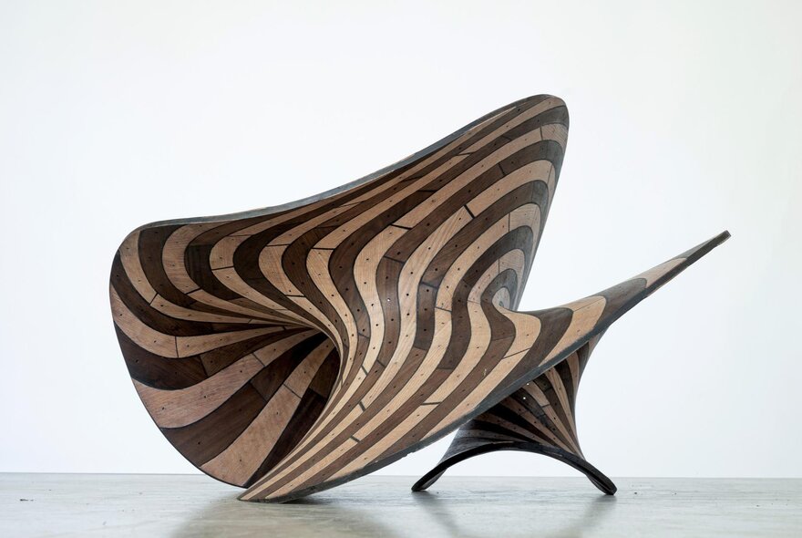 A wooden sculpture with flowing stripes made from dark and light wood.