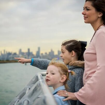 A mother and two young children on the deck of a ferry looking out across the water.