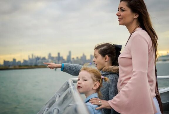 A mother and two young children on the deck of a ferry looking out across the water.