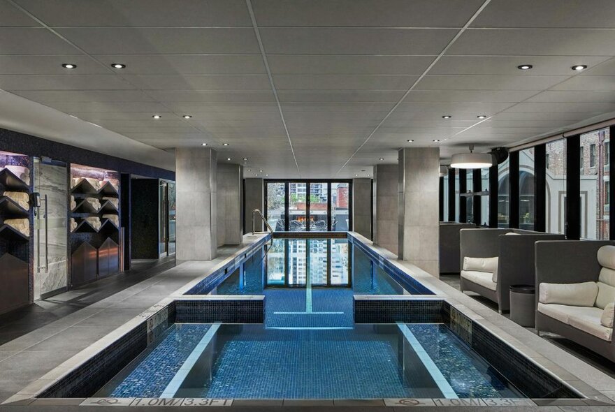 Hotel spa area with spa pool and lap pool surrounded by cushioned sofas and equipment.