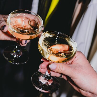 Two hands bringing cocktail glasses together.