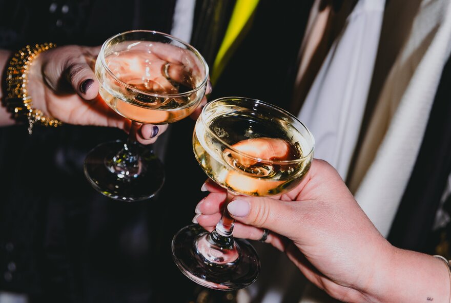 Two hands bringing cocktail glasses together.