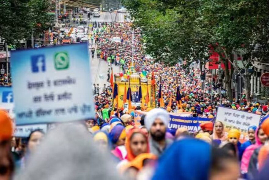 A large crowd of people in bright colours marching down a street with placards. 