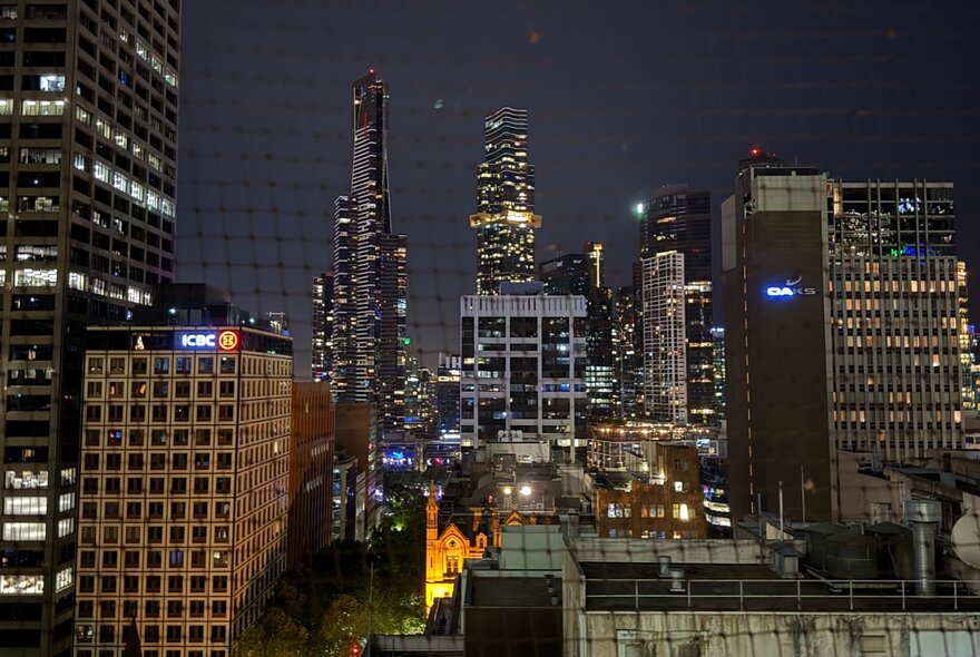 View of the Melbourne city skyline at night from a balcony with a small round table.