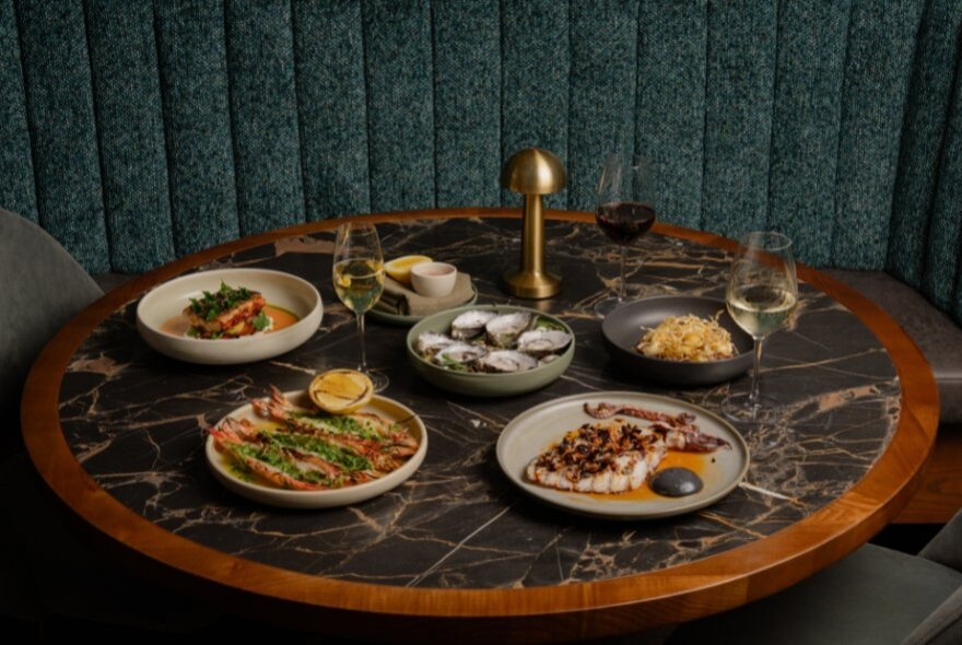A round table with five gourmet dishes displayed on it, in front of a moss green banquet seat.