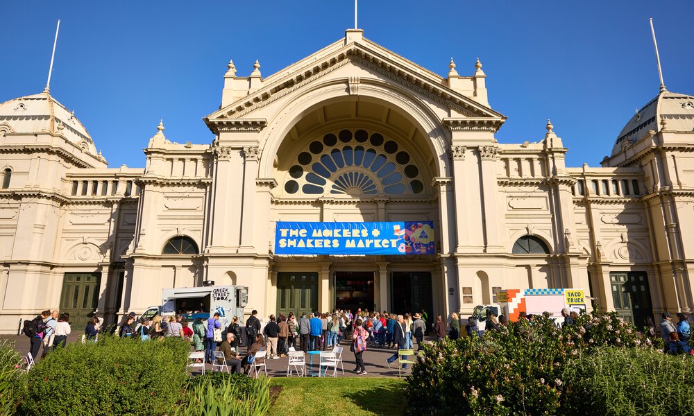A crowd of people standing outside a large exhibition building on a sunny day.