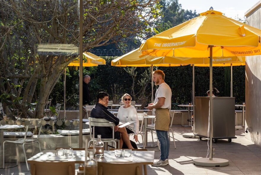 The outdoor courtyard at The Observatory, with tables and chairs arranged under yellow shade umbrellas.