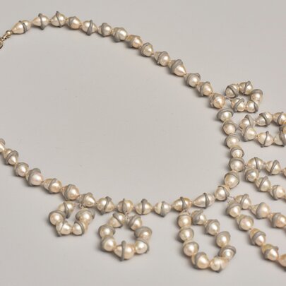 An asymmetrical pearl necklace featuring unique, double-pointed pearls arranged in a single strand that cascades into decorative loops and rings along one side.