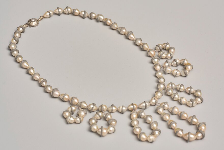 An asymmetrical pearl necklace featuring unique, double-pointed pearls arranged in a single strand that cascades into decorative loops and rings along one side.