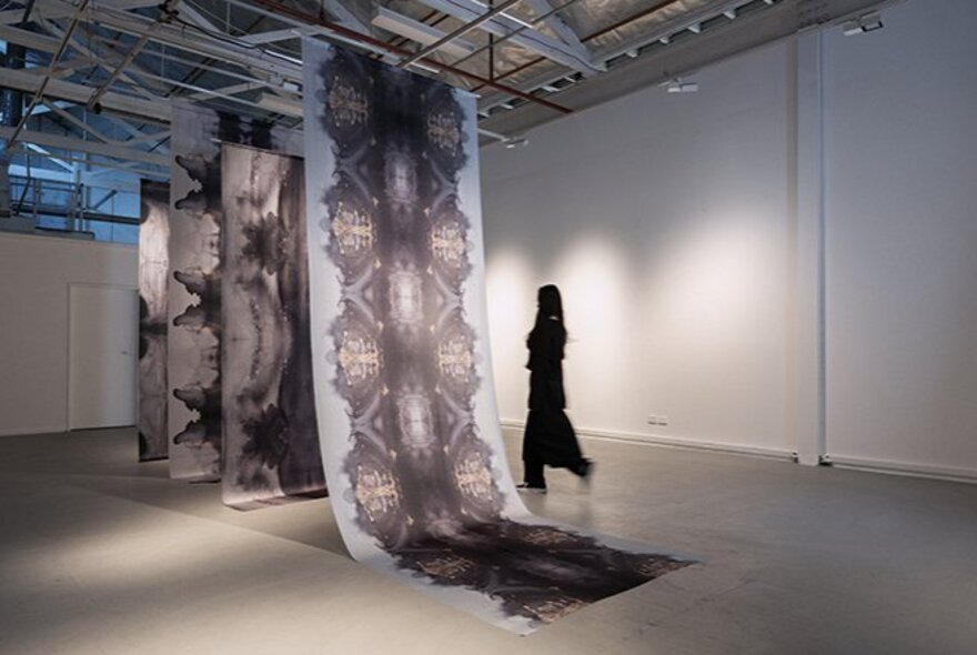A contemporary art gallery installation featuring large-scale fabric hangings with a person walking past them. 