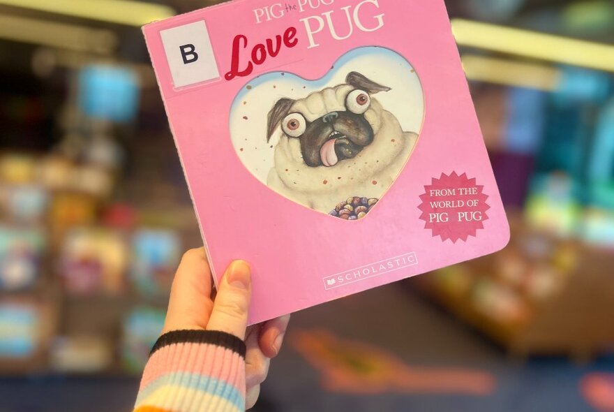 A hand holding up a pink Pig the Pug book.