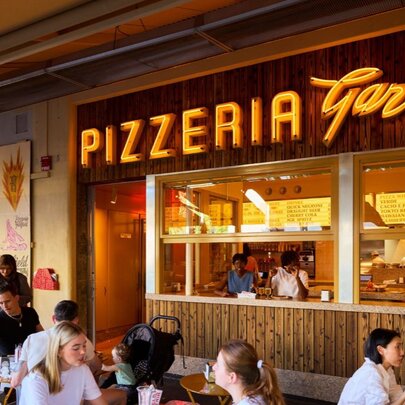 Customers dining outside under an awning at a pizzeria.