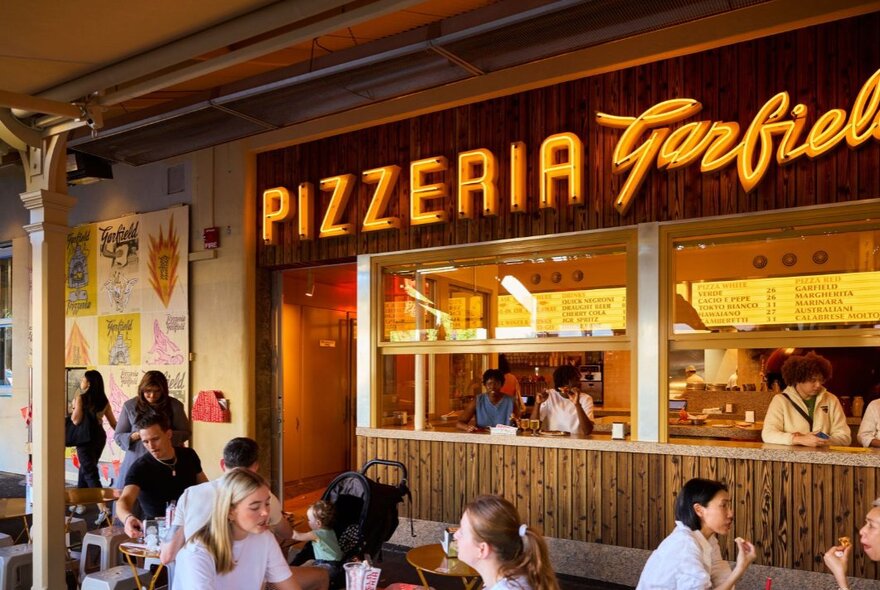 Customers dining outside under an awning at a pizzeria.