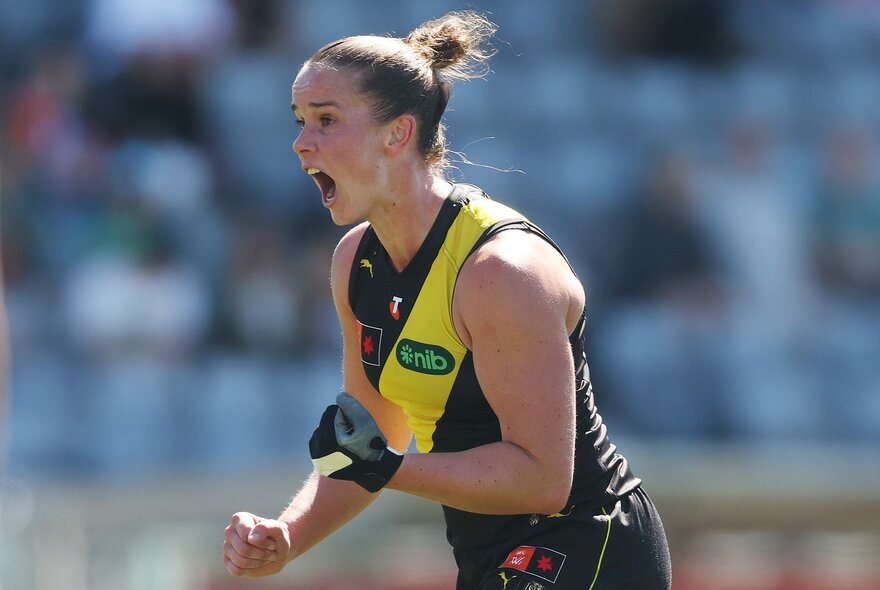 A Richmond AFLW player celebrating and cheering herself on the field with clenched fists.