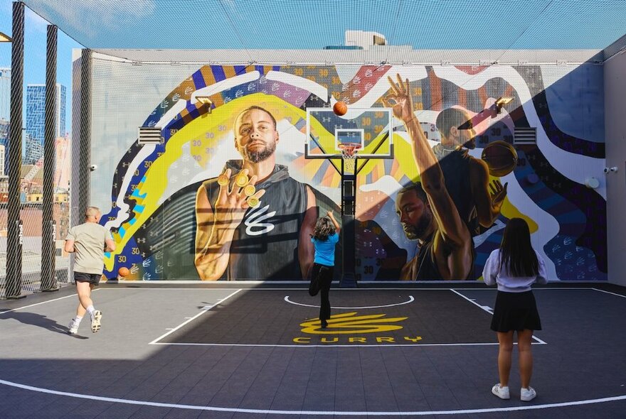 An outdoor basketball court at Rebel Emporium in the Melbourne CBD, with kids shooting hoops in front of a large mural. 