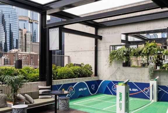 A small blue Pickleball court in the outdoor area of Rooftop at QT, with city buildings in the background.