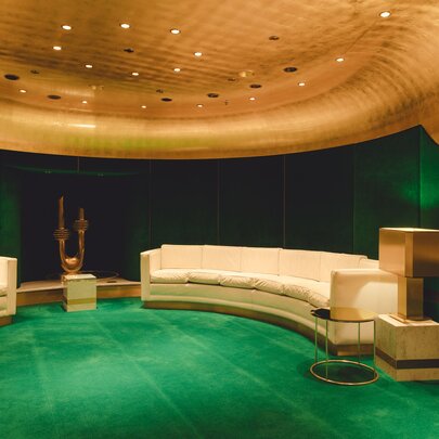 The lush interior of a small, private theatre in the Melbourne Arts Centre, with emerald green carpet and darker green walls, gold ceiling and curved cream lounges.