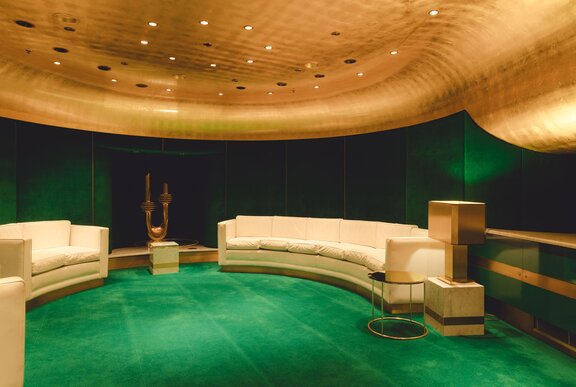 The lush interior of a small, private theatre in the Melbourne Arts Centre, with emerald green carpet and darker green walls, gold ceiling and curved cream lounges.