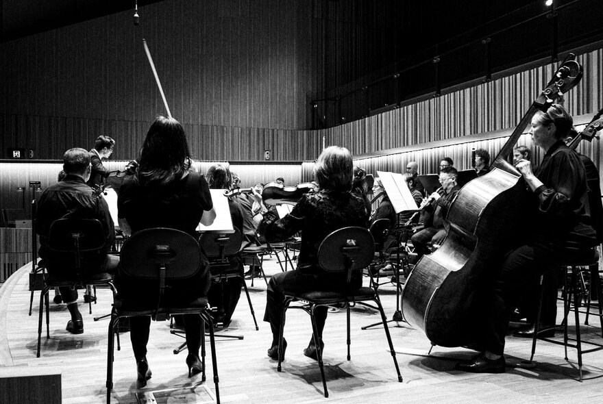Black and white image of seated members of Orchestra Victoria taken from the side of the stage.