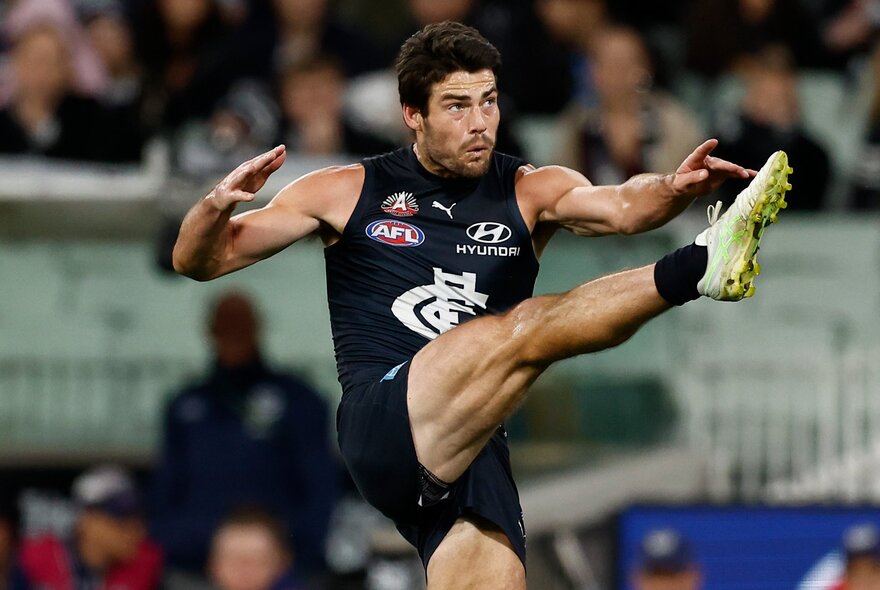 Carlton AFL football player kicking the ball during a match, his leg in mid-air.