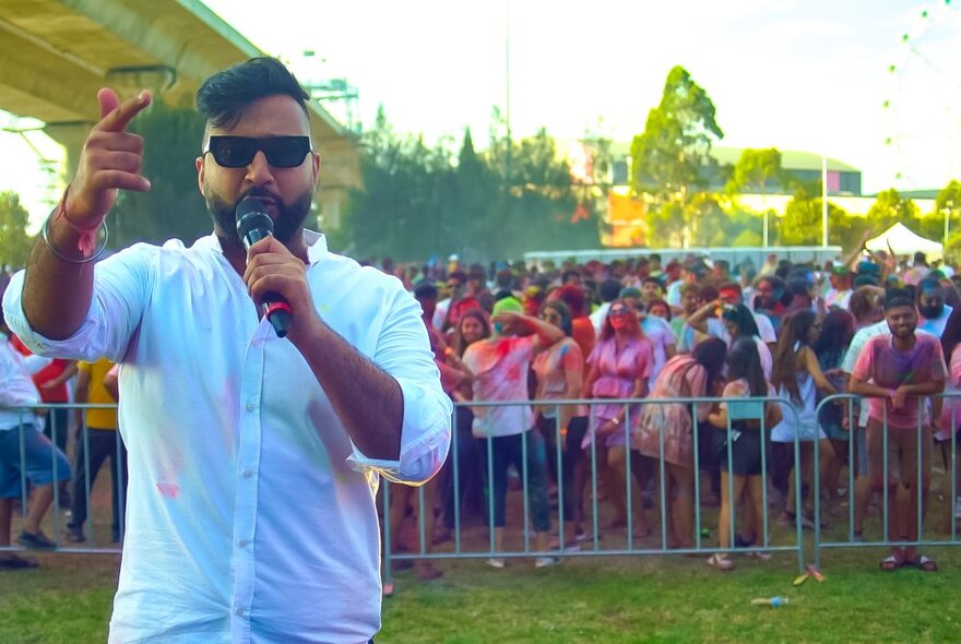 A man with a microphone speaking with a crowd behind a barrier at the back of him. 