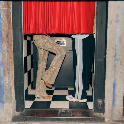 A vintage-style photo booth with red curtains and two sets of legs visible underneath them.